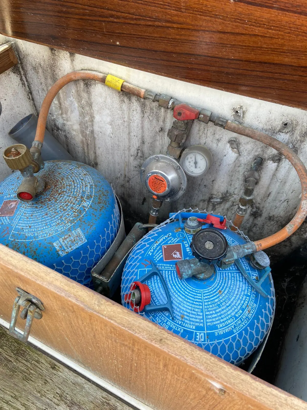 Zwei blaue Gasflaschen mit Druckregler und Schläuchen in einem geöffneten Stauraum an Bord