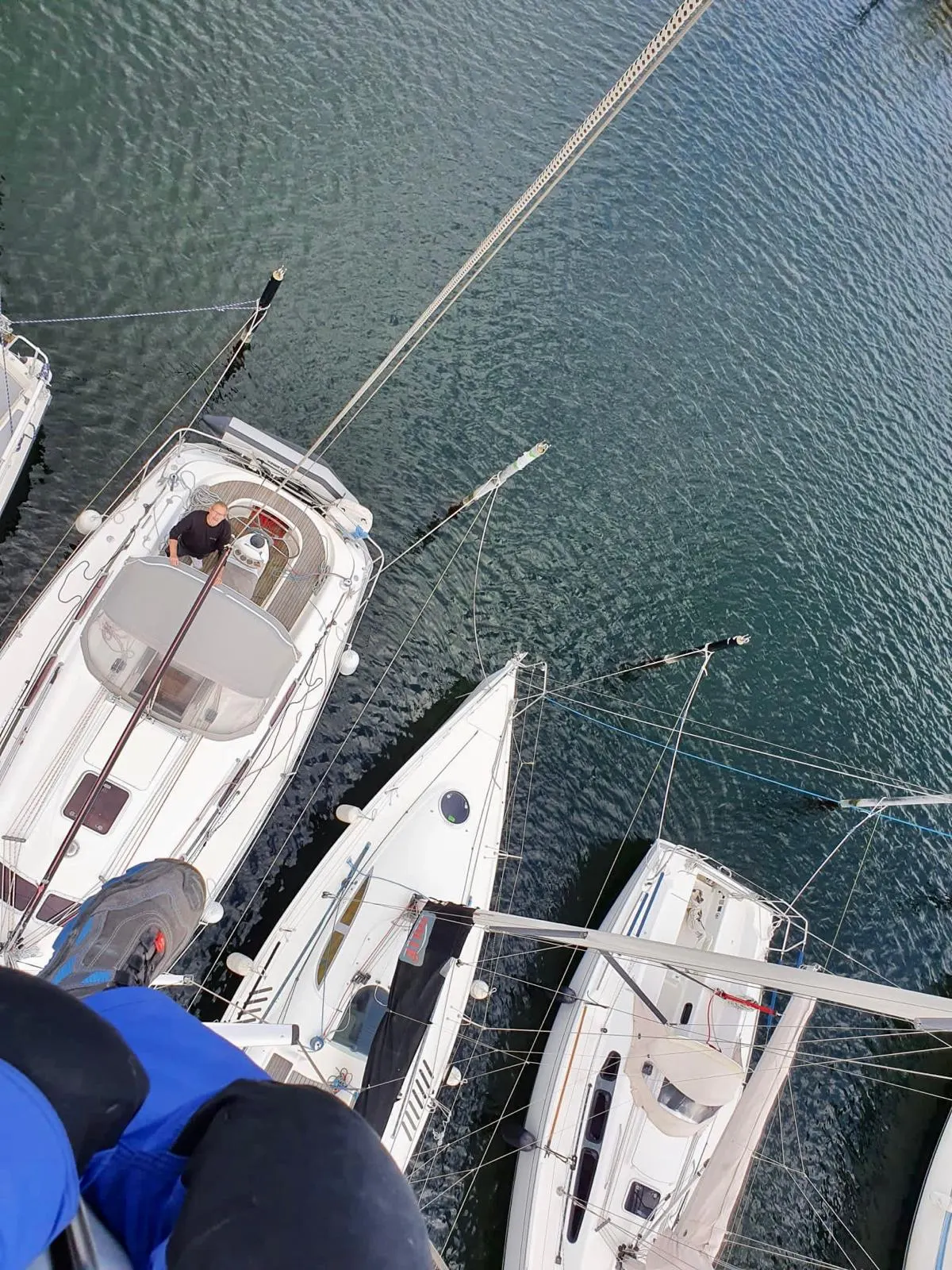 Blick von oben aus dem Mast auf das Deck eines Segelboots, eine Person schaut nach oben