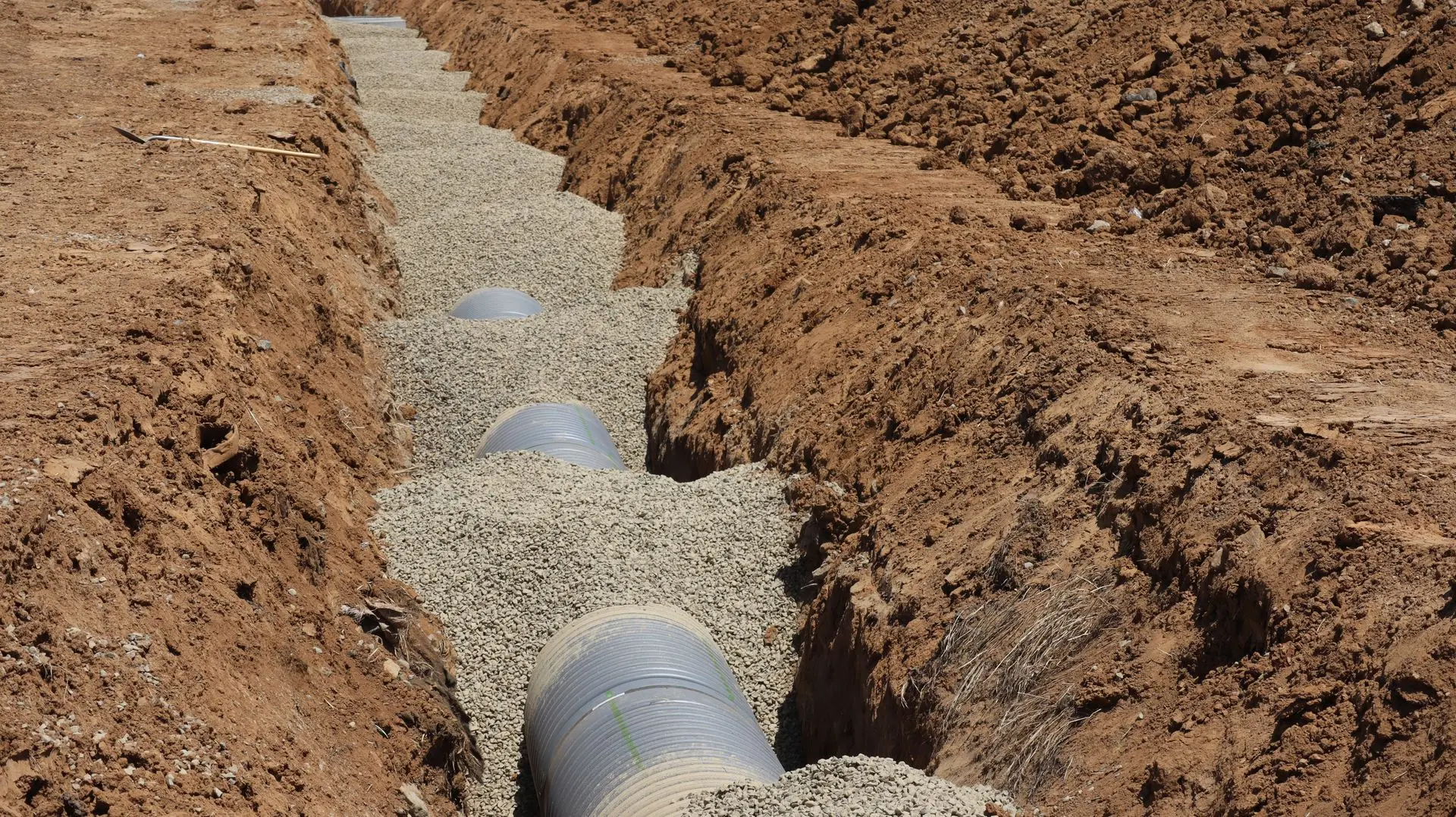 Offener Rohrgraben mit frisch verlegten Abwasserrohren auf einer Baustelle